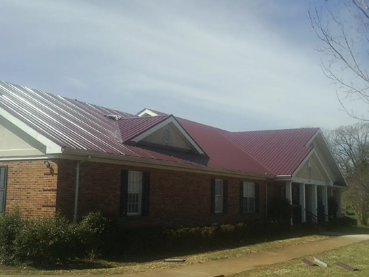 Red metal roof with gabled entries on a long brick building, from a Hail Damage Roof Repair job in Winston