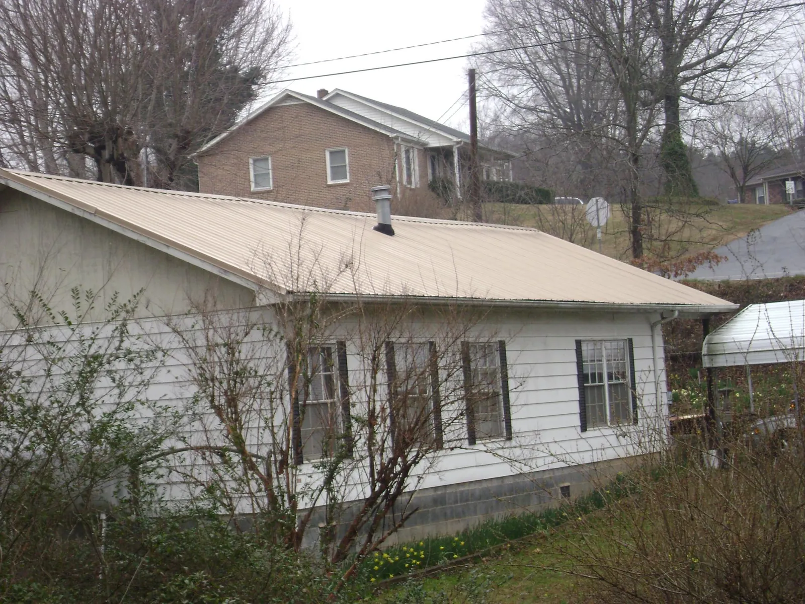 Tan metal roof on a white sided house set into a hillside — Commercial Roofing by Roofing Brothers in Winston